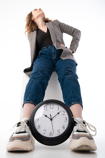 Deadline concept, time management. A woman holds between her legs a large clock on a white background.