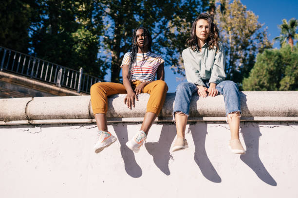 istock Two multiethnic women sitting on a urban wall. 1395386645