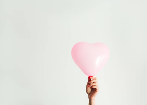 istock Pink inflatable heart-shaped balloon in hand. White background. 1395392481