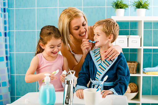 Mother helping child to properly brush his teeth in the bathroom