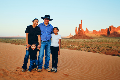 A Navajo family standing on the sand in Monument Valley at sunset.