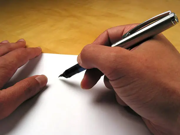 Photo of Hands holding a fountain pen over a blank sheet of paper