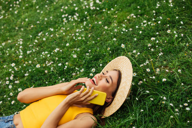 istock Smiling young woman lying on grass and using smartphone 1395398322