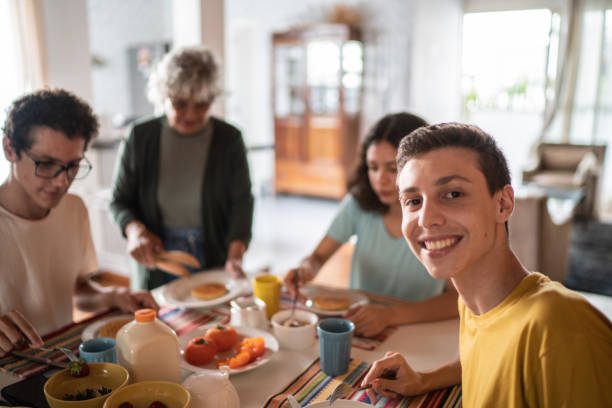 retrato de un joven desayunando con la familia en casa - cousin fotografías e imágenes de stock