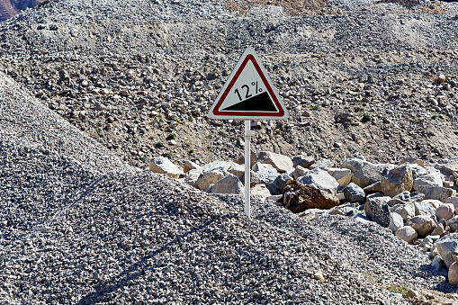 road sign on the pole warning about a steep ascent half covered with rubble during road construction