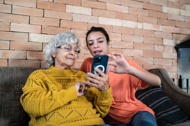 nieta ayudando a la abuela a usar el teléfono móvil en casa - grandmother generation gap senior adult granddaughter fotografías e imágenes de stock