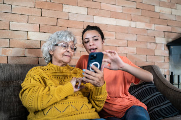 nipote che aiuta la nonna a usare il cellulare a casa - divario generazionale foto e immagini stock