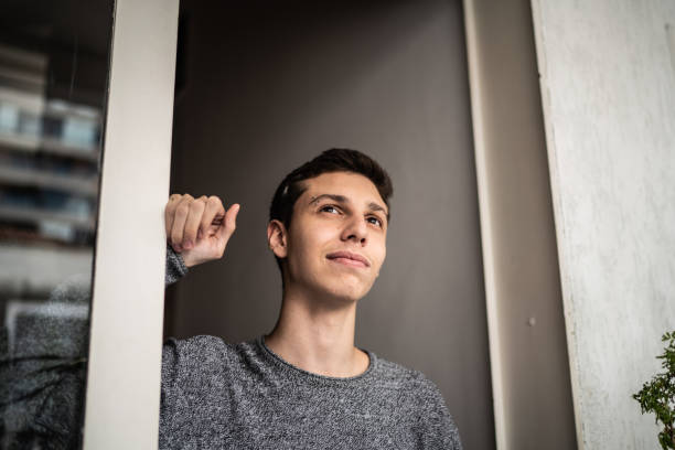 Contemplative young man looking through window at home