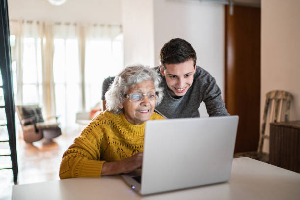 grandson and grandmother using laptop at home - grandparent senior adult senior women multi generation family imagens e fotografias de stock