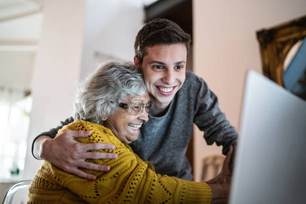 nipote e nonna che abbracciano e usano il laptop a casa - grandparent adult smiling looking at camera foto e immagini stock