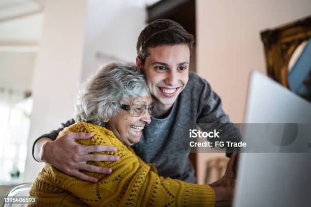 Grandson And Grandmother Embracing And Using Laptop At Home Stock Photo - Download Image Now