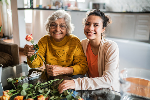Portrait of happy senior woman and her granddaughter preparing flower vase at home