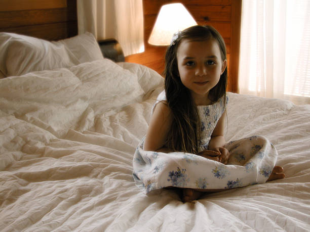 Sitting Pretty Little girl sits with her legs crossed  and hands in lap on a bed and smiles.  positive discipline in kids stock pictures, royalty-free photos & images