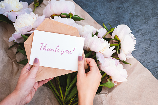 Thank you card in hands, message, envelope, pink peony flowers bouquet