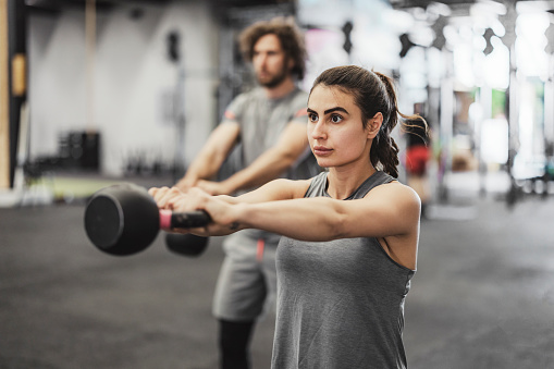 Shot of two sporty young people exercising with kettlebells in a gym