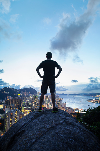 Man standing with arms on waist on top of rock formation in nature, Hong Kong, China, from Braemar Hill Peak
