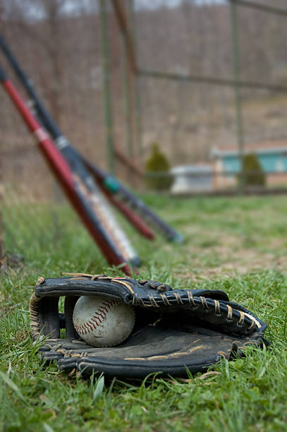 Baseball and Glove A baseball and glove laying in the grass with baseball bats in the background. left handed catcher stock pictures, royalty-free photos & images