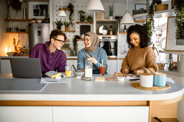 Group of friends having breakfast together Group of university students having breakfast together in the morning in their apartment. Young man using laptop for studying and doing his school project. roommate stock pictures, royalty-free photos & images