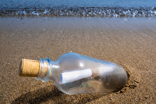Closeup of a glass bottle with a message in the sand of a beach.