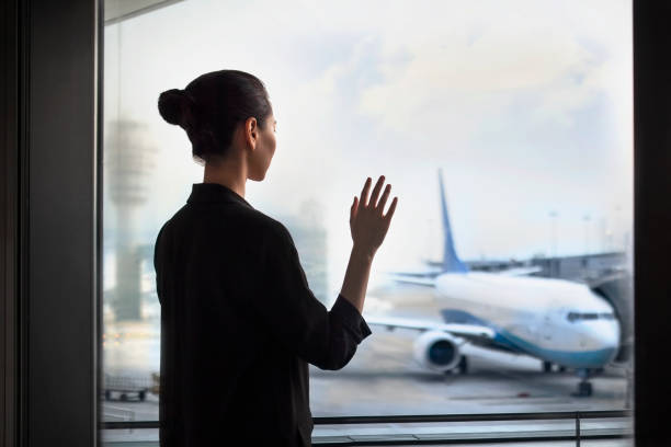 Young Chinese woman standing at airport terminal departure area waving to airplane stock photo