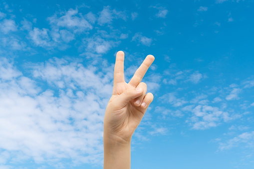 Peace sign gesture made by child on blue idyllic sky background. World peace concept.