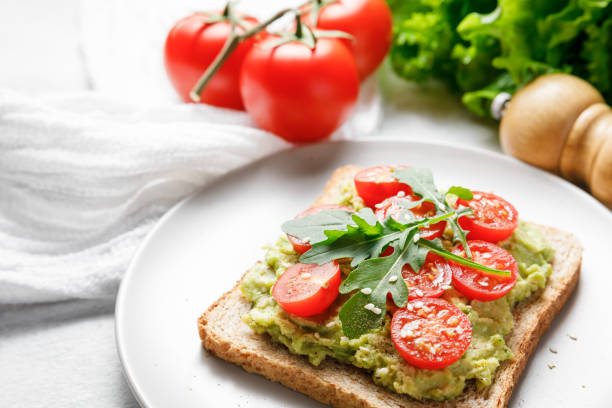 istock Avocado rye bread toast with cherry tomatoes and arugula on bright background. Healthy appetizer, breakfast, lunch or snack. Vegan food concept. Close up 1395432979