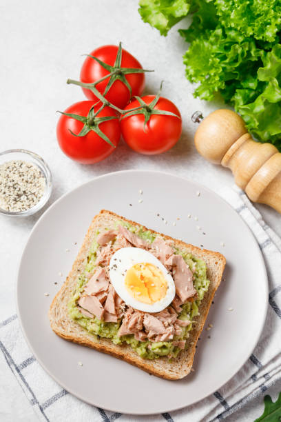 istock Avocado rye bread toast with tuna and boiled egg on bright background. Healthy appetizer, breakfast, lunch or snack. Top view 1395432986