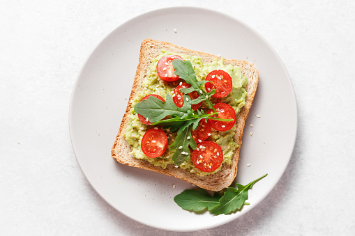 Avocado rye bread toast with cherry tomatoes and arugula on bright background. Healthy appetizer, breakfast, lunch or snack. Vegan food concept. Top view.