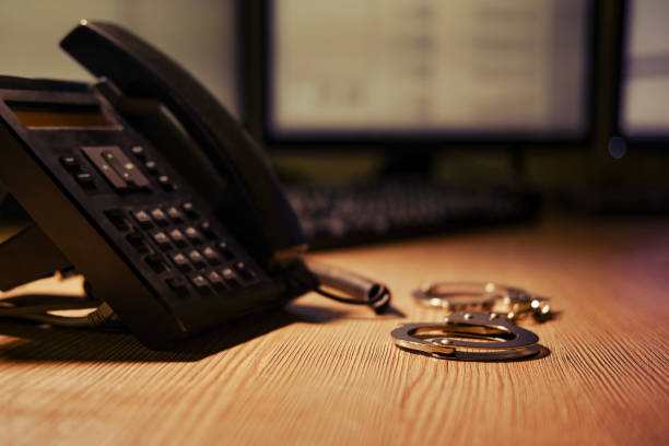 Landline phone and handcuffs on the table, close-up. Office desk in a dark night room with computer monitors Landline phone and handcuffs on the table, close-up. Office desk in a dark night room with computer monitors synthetic identity theft stock pictures, royalty-free photos & images