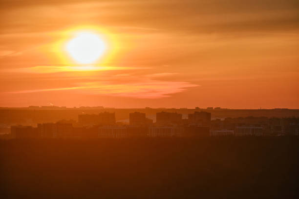 morgensonne durch bewölkte wolken an einem heißen, nebligen himmel über silhouetten von stadtgebäuden, roter sonnenaufgang. morgendämmerung in dunstwolken über häusern in der stadtlandschaft - heat haze fotos stock-fotos und bilder