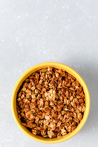 Homemade oatmeal granola bowl with spoon on ligth grey background. Healthy breakfast concept. Organic oat, almond and sunflower seeds. Top view, flat lay, copy space
