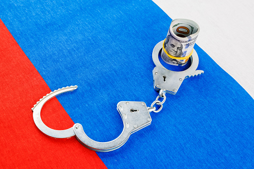 roll of us dollar banknotes in a handcuffs on flat full-frame russian flag, closeup