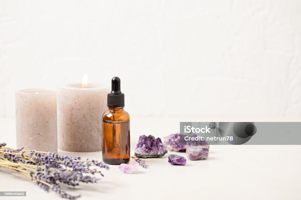 Glass bottle of Lavender essential oil with lavender flowers and candles and amethyst crystals. Meditation, zen, aromatherapy,spa massage concept Essential Oil Stock Photo