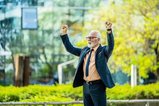 Cheerful mature businessman celebrating his success while standing outdoors in the city.