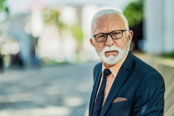 Portrait of shocked senior businessman having a discussion with someone and looking at camera while sitting outdoors in the city.