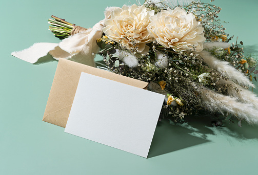 Dried flower bouquet and blank message card placed on green background. Wedding and celebration concept.