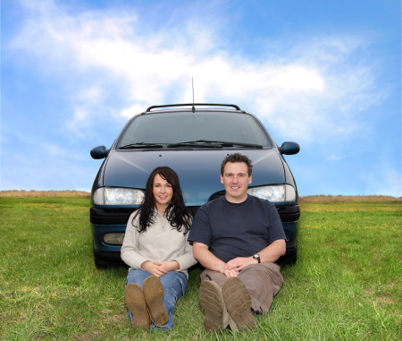 Couple sitting in front of a car outdoors.