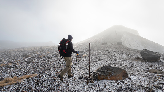 Hiking the steep scree terrain to the Red Crater summit in the heavy fog on Tongariro Alpine Crossing. New Zealand.