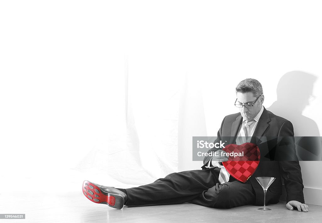 Heart and SOLE Valentine Man in business suit holds candy heart box while sitting on floor beside martini glass. Both heart and sole (soul) are red.. rest is black and white. Lots of room for copy. Box - Container Stock Photo