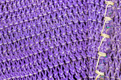Purple fishing net hanging, stretched to dry on harbor dock, stitches, full frame close-up view suitable for background purposes.  Muros, A Coruña province, Galicia, Spain.