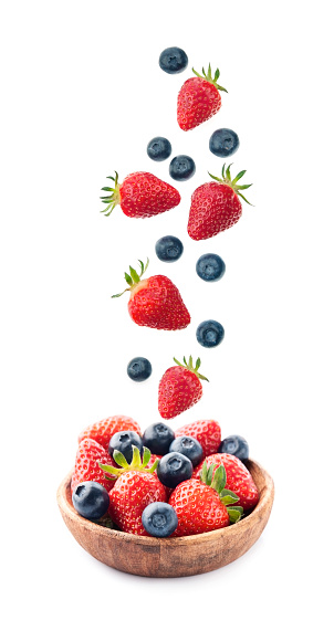 Falling berries of strawberry and blueberry on wooden bowl isolated on white backgrounds.
