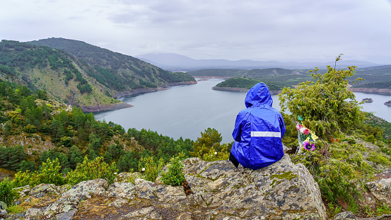 Man sitting on a rock high in the mountains and watching the rainy landscape