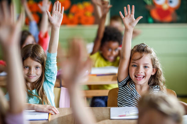 istock Happy school children raising their hands to answer the question on a class. 1395468278