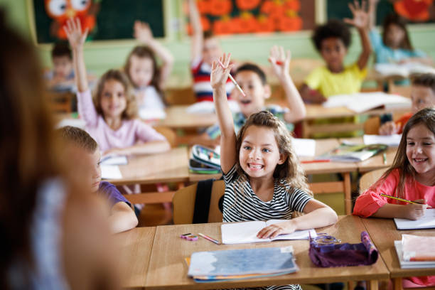 istock Group of happy elementary students raising their arms in the classroom. 1395468529