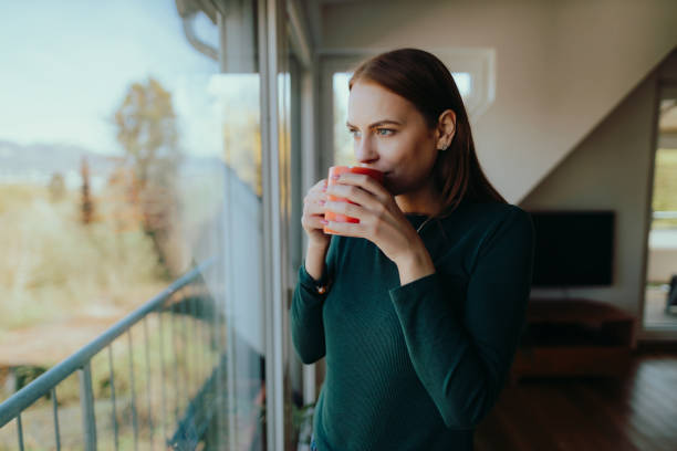 donna che beve caffè e guarda attraverso la finestra - waking up window women morning foto e immagini stock