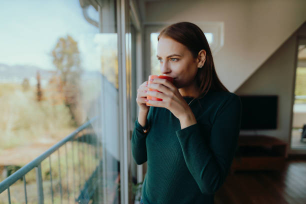 женщина пьет кофе и смотрит в окно - waking up window women morning стоковые фото и изображения