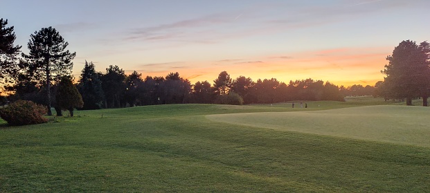 a panoramic scene of an empty golf course , with the shadows falling toward camera as the light fades .