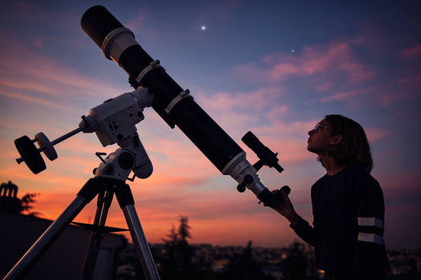 istock Girl with astronomical telescope stargazing under twilight sky. 1395472079
