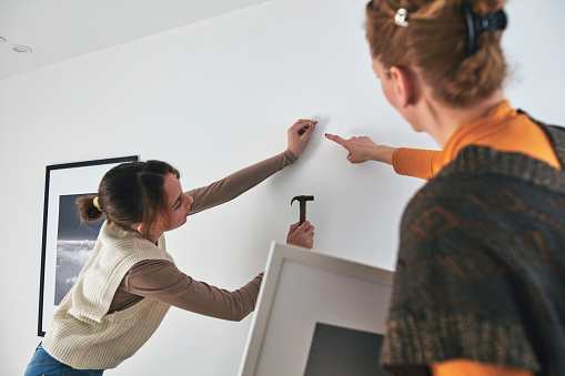 Mother and daughter hanging pictures and photos at home.