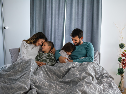 Happy family relaxing together in bed playing and laughing